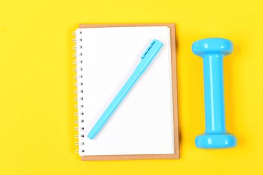 Sarı arkaplanda defter, kalem ve spor aletleri üst görünümü
