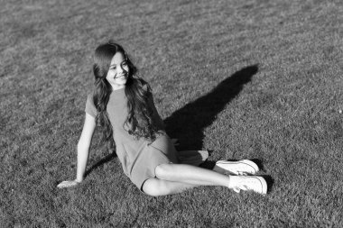 Çocuğu ne mutlu eder? Yaz tatili. Tatil fikirleri. Mutlu gülümseyen kız çimenlerde rahatlamayı sever. Neşeli bir kız öğrenci. Eğlenmene bak. Şirin kız yeşil çimlere oturuyor. Duygusal olarak mutlu çocuk dışarıda dinleniyor.