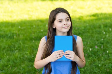Günde bir kitap can sıkıntısını uzak tutar. Küçük kız kitabı açık havada tutuyor. Yaz günü küçük bir okuyucu. Kütüphane kitabı. Fantezi ve kurgu. Edebiyat ve şiir. Okuma alışkanlığı. Kutsal kitapta kaybolun.