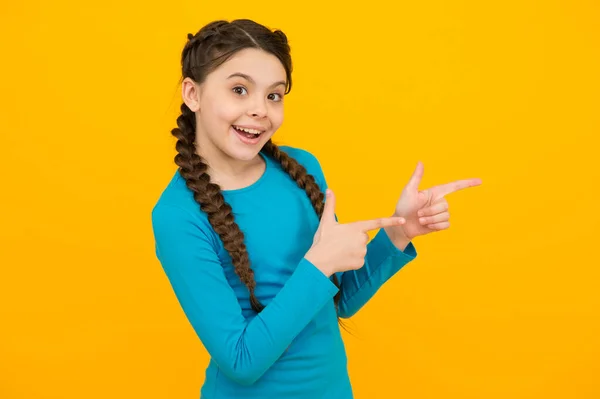 Mira eso. joven hermosa chica sonriente con peinado de moda. Niño sobre fondo amarillo, espacio para copiar. Emociones positivas. Peluquería infantil aquí. Retrato de chica feliz señalando con el dedo — Foto de Stock