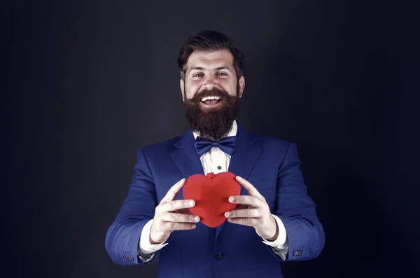 O amor está no ar. brutal hipster barbudo em roupa formal. homem de negócios bem sucedido confiante em terno com gravata borboleta. Feliz Dia dos Namorados. Homem de smoking com coração vermelho. amor e romance. pronto para data — Fotografia de Stock