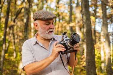 Doğal ışık kullanarak fotoğraf çekimi. Son sınıf öğrencisi, sonbahar günü fotoğraf çekiyor. Eski fotoğrafçı fotoğraf makinesini tutar. Manzara ve doğa fotoğrafı çekimi. Hobi ya da meslek etkinliği