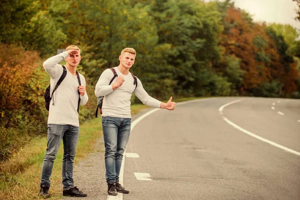 Missed their bus. Need help. Cheap transport. Transport problem. Try to stop some car. Travel and transport concept. Twins men at edge of road nature background. Reason people pick up hitchhikers
