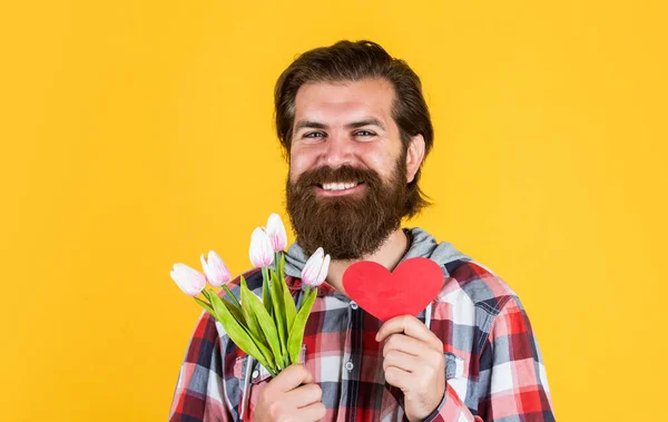 Готовий до романтичного побачення. подарунок для жінок і матерів. щасливий бородатий чоловік тримає квіти тюльпанів і декоративне серце. святкування дня святого Валентина. З днем народження подарунок з любов'ю. весняний букет для неї — стокове фото