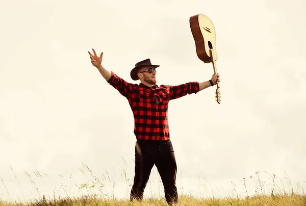 Inspired country musician. Country style. Summer vacation. Hiking song. United with nature. Handsome man with guitar. Country music concept. Guitarist country singer stand in field sky background