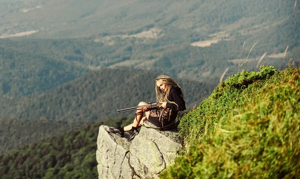 Concetto mirato. Stagione di caccia. Hunter montagne paesaggio sfondo. Guerriero sexy. Donna attraente capelli lunghi bel viso tenere fucile per la caccia. Amazon ragazza sedersi sulla scogliera preparare pistola per la caccia — Foto Stock