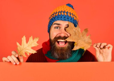 Heyecanlı yüzü olan adam turuncu arka planda kalın bir şapka takıyor.