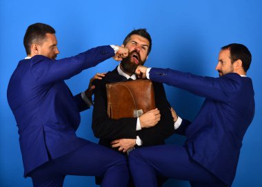 Sakallı ve ciddi yüzlü adamlar evrak çantalı adamı yumrukluyor..