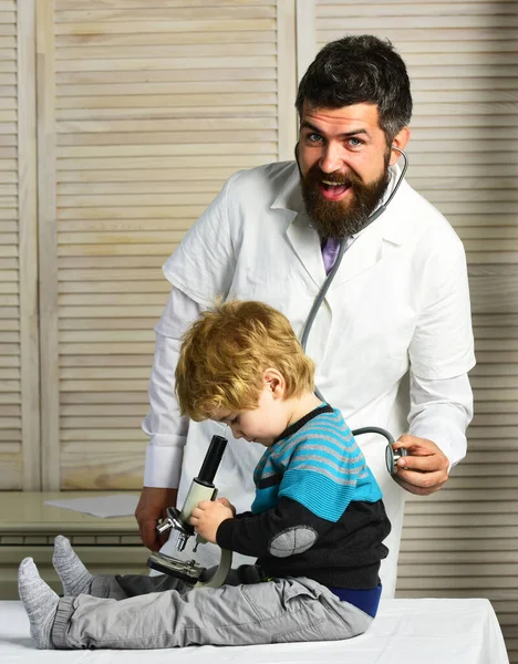 Hombre examina niño sentado en la mesa sobre fondo de madera . — Foto de Stock