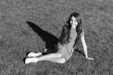 Küçük ve güzel. Mutlu küçük kız yeşil çimlere oturur. Küçük çocuk yaz elbisesi giyer. Sevimli küçük bebek gülüşü açık havada güneşli. Güzellik ve moda. Yaz zamanı. Tatil