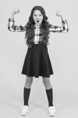 Bir kız olmanın gücünü hissetmek. Güçlü kız sarı arka plan. Küçük kız kollarını esneterek gücünü göster. Okul üniformalı moda kızı görünüşü. Sağlık ve güç. Okul modasına geri dönelim. Resmi biçim