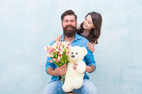 Här för att fira dig. Glad familj firar födelsedag. En liten flicka gratulerar skäggig man. Liten dotter och far håller blommor och leksak. Födelsedag. Grattis på födelsedagen. — Stockfoto