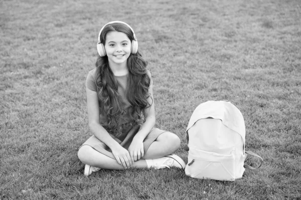 Dziewczęce słuchawki słuchające muzyki. Nowoczesna technologia. Uczennica lubi melodię. Słuchaj muzyki relaksującej na świeżym powietrzu. Dziewczynka cieszyć się muzyką zielonej trawy łąki. Przyjemny czas. Słuchawki dla dzieci słuchają muzyki — Zdjęcie stockowe