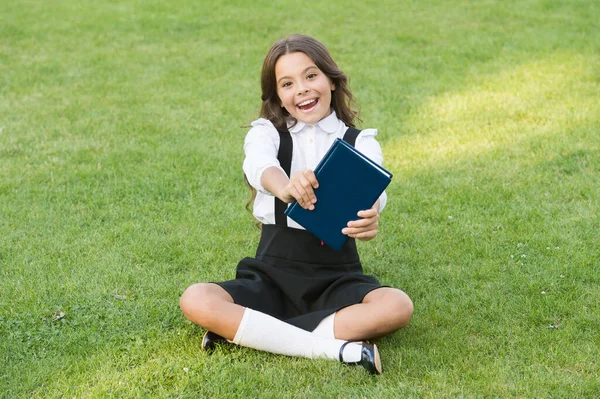 教育のための素晴らしい場所。女の子は本を読んでる。子供のための文学。子供の頃の記憶を。ノートにメモを。学校に戻って。公園で勉強してる。本で緑の芝生でリラックスして — ストック写真