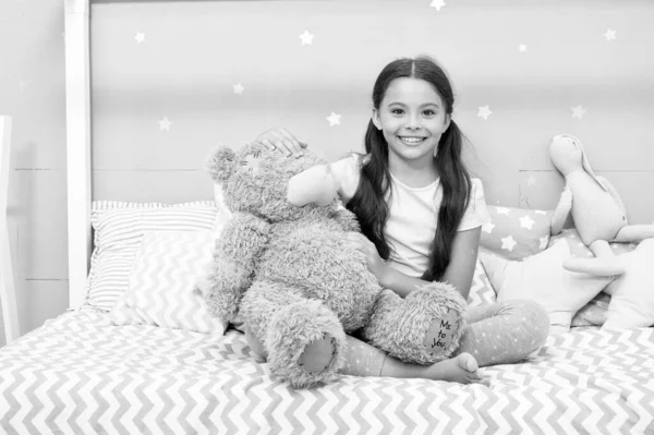 Denkbeeldige interactie. Speel spelletjes. Favoriete speeltje. Meisje knuffel teddybeer in haar slaapkamer. Aangename tijd in gezellige slaapkamer. Meisje kind lang haar schattig pyjama ontspannen en spelen pluche teddy beer speelgoed. — Stockfoto