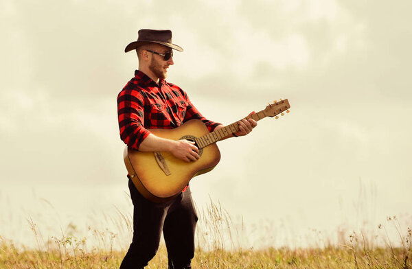 Inspired country musician. Country style. Summer vacation. Country music concept. Guitarist country singer stand in field sky background. Hiking song. Play beautiful melody. Handsome man with guitar