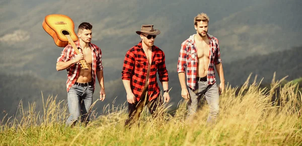 Tourists hiking concept. Hiking with friends. Enjoying freedom together. Long route. Group of young people in checkered shirts walking together on top of mountain. Men with guitar hiking on sunny day