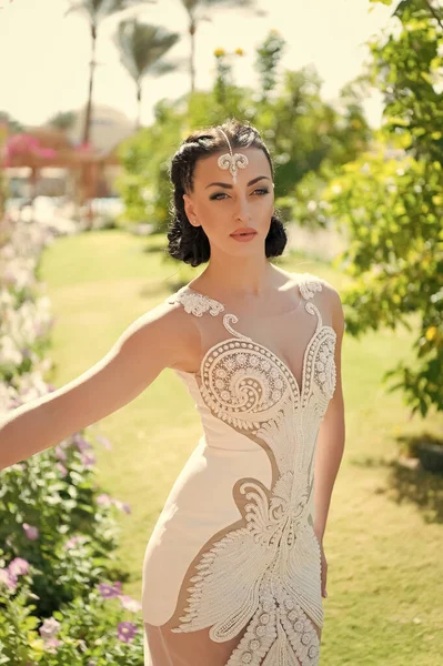 Elle est parfaite. Fille accessoire robe de luxe attrayant. Dame en tenue de luxe promenades exotique fond de jardin. Femme maquillage coiffure porte robe ajustée serrée à la mode avec broderie et perles — Photo