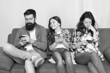 Anne baba ve kızı kanepede dinleniyor. Aile hafta sonunu internette geçiriyor. Küçük bir kız çocuğu, ailesine karşı akıllı telefon kullanıyor. İnternette aile sörfü. Aile eğlencesi. Oyun uygulaması oynat. Çevrimiçi aile