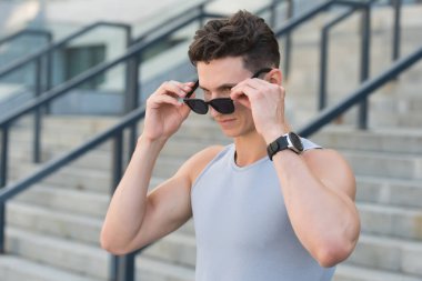 Şık bir spor modası ve güneş gözlüğü. Yakışıklı adam spor kıyafetler giyiyor. Saati olan bir sporcu. Fitness erkek sporcusu dışarıda antrenman yapmaya hazır. Erkek spor modası. Güçlü ve kaslı.