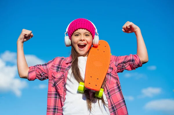 Flickkraft. Glad skridskoåkare flex armar på blå himmel. Ett litet barn med penny board utomhus. Ett strömglidtrick. Friktionslekplats. Energiskateparken. Skateboardåkning. Rolig fysikverksamhet — Stockfoto