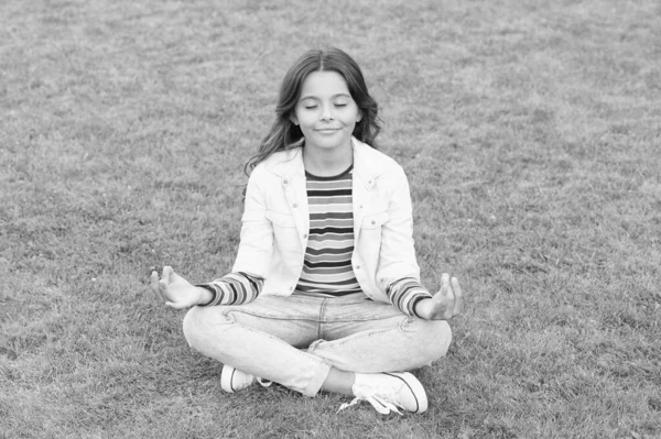 Ребенок медитирует в позе йоги на траве. ребенок в позе лотоса на зеленой траве. Концепция спокойствия и медитации. медитация в природе. Спокойствие и покой. маленькая девочка медитирует в летнем парке. здоровый образ жизни — стоковое фото