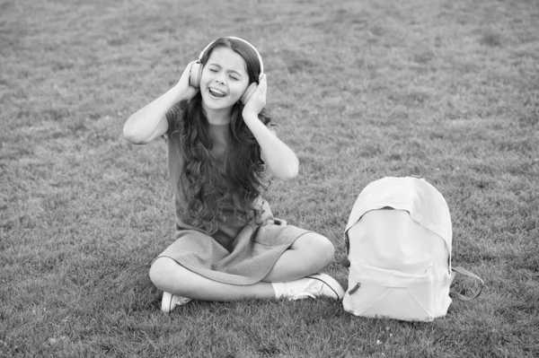 女の子のヘッドフォン音楽を聞いて。楽しい時間だ。子供のヘッドフォンは音楽を聞く。現代の技術。女子高生はメロディーを楽しむ。屋外でリラックスして音楽を聞く。子供の女の子は音楽を楽しむ緑の草の牧草地 — ストック写真
