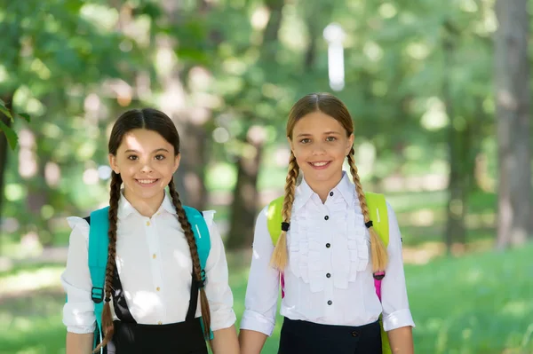 Niños adolescentes felices llevan mochila. de vuelta a la escuela. niñas de la escuela pequeña caminando en primavera. Feliz día de los niños. felicidad infantil. dos hermanas en uniforme escolar al aire libre. listo para las vacaciones — Foto de Stock