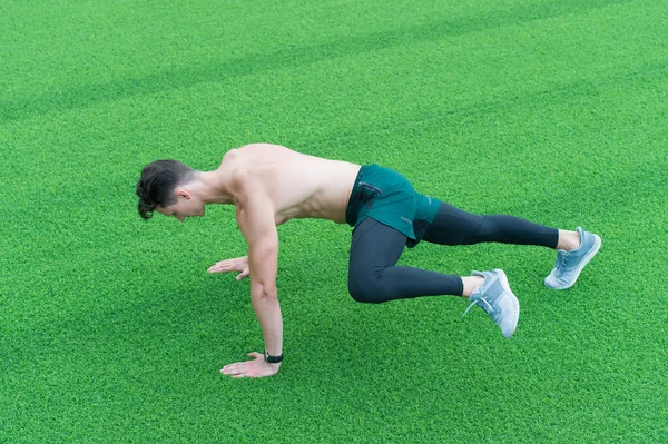 Atletický muž cvičí na prkně. svalnatý sportovec trénující v zelené trávě. Utíkej, jak dýcháš. Sportovec tvrdě trénuje své spodní a horní části těla na trávě. Školení na čerstvém vzduchu — Stock fotografie