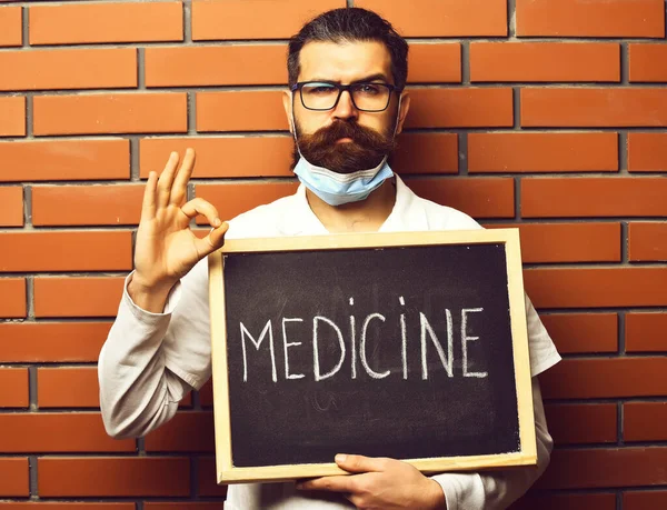 Barbudo brutal caucasiano médico segurando bordo com medicina inscrição — Fotografia de Stock