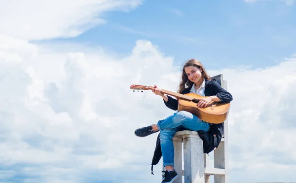 音楽学校の授業。空を背景に小さなギタープレーヤー。カントリー・ミュージックのスタイル。弦楽器。アコースティックギターで演奏する。女の子は音楽が好きなんだ。コピースペース — ストック写真