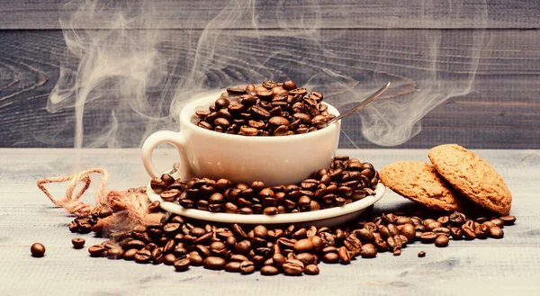 Káva pro inspiraci a nabití energií. Šálek plný kávy hnědé pražené fazole bílé mraky kouře modré dřevěné pozadí. Stupeň pražení obilí. Jídlo v kavárně. Čerstvé pražené kávové zrno — Stock fotografie