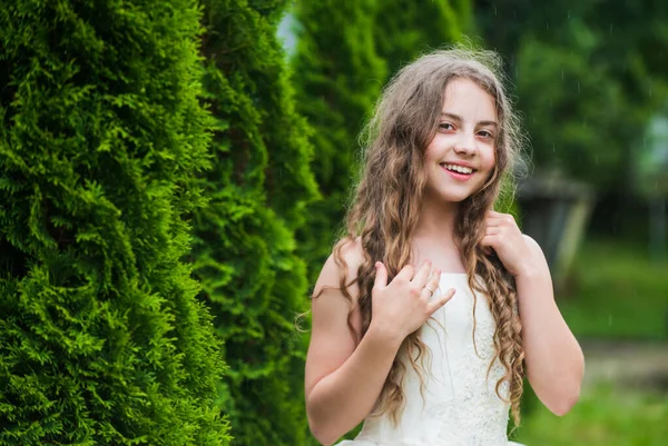 Happy moments. small girl with long curly hair. little beauty in white dress. wedding angel kid. child enjoy park with thuja. spring cypress tree. summer nature. female hairdresser fashion — Stock Photo, Image