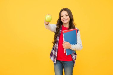 Meyveli çerez görünüşünü değiştirecek. Mutlu çocuk elma tutuyor ve kitaplar sarı arka planda. Okul tatili. Bilginin meyvesi. Beslenme ve sağlık eğitimi. Sağlıklı yiyecekler. Besleyici ol.