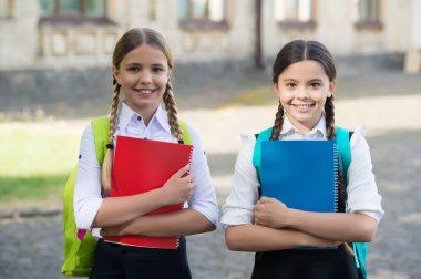 Ders çalışırken iyi eğlenceler. Okul üniformalı mutlu kızlar. Sırt çantalı gülümseyen genç öğrenciler. İlkokulda eğitim. Öğrenci kızlar birlikte ders alıyorlar.