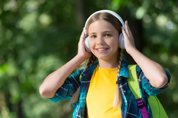 どこへ行ってもヘッドフォンを取りなさい。幸せな子供は屋外で自然なヘッドフォンを着用します。音楽を聴く。楽しさとエンターテイメント。新しい技術だ。夏休みだ。ヘッドフォンを親友にする — ストック写真