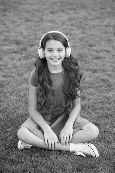教育用ポッドキャスト。子供の女の子は音楽の緑の草の牧草地を楽しむ。楽しい時間だ。私の夏のプレイリスト。屋外でリラックスしながら音楽を聴く。子供のヘッドフォンは音楽を聞く。女の子のヘッドフォン｜リスニングミュージック — ストック写真