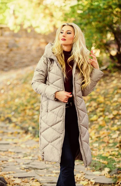 Dziewczyna modny spacer blondynka w jesiennym parku. Kobieta nosi ciepłą szarą kurtkę. Kurtka, którą każdy powinien mieć. Zróżnicowany trend kurtki. Jak kołysać kurtkę buforową jak gwiazda. Koncepcja trendu mody puffer — Zdjęcie stockowe