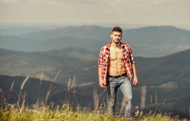 Yürüyüş kaslı gövdesi dağ zirvesine ulaşır. Yürüyüş konsepti. Adam dağ manzarasının tepesinde duruyor. Sporcu adam dağları gevşetiyor. Güzel bir çevre. Kaslı turist dağ yamacında yürüyor