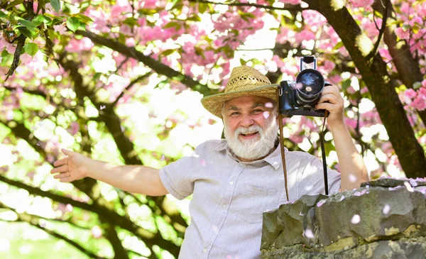 Senior man hold professional camera. Retirement travel. Spring holidays. Travel photo. Photographer in blooming garden. Enjoying free time. Travel and tourism. Capturing beauty. Happy grandfather — Stock Photo, Image