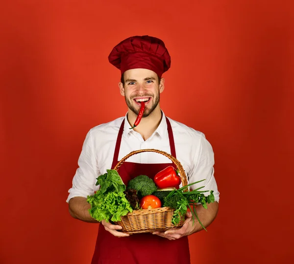 Chef en uniforme borgoña sostiene chile rojo en la boca. —  Fotos de Stock