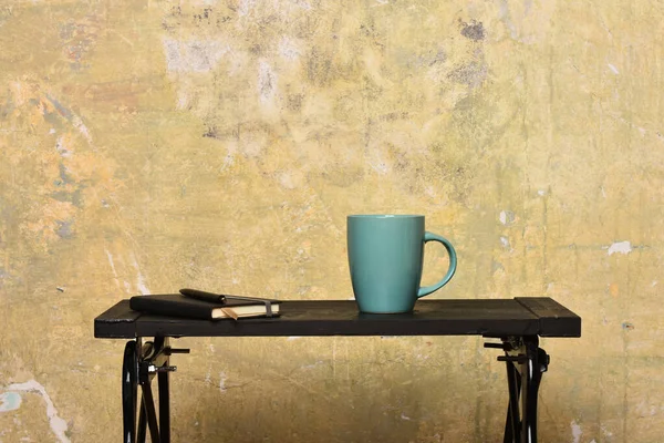 Cuaderno con marcador, bolígrafo y taza azul en la mesa cerca de la pared. — Foto de Stock