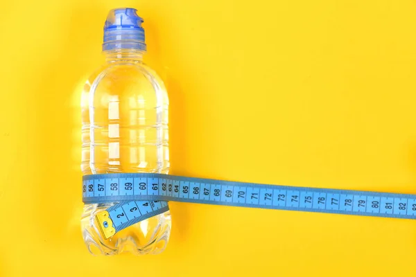 Botella de agua y aparatos de fitness sobre fondo amarillo — Foto de Stock
