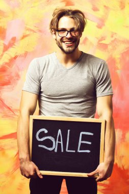 Beyaz sakallı seksi maço adam elinde satılık bir yazı tutuyor.