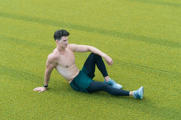 Een gespierde kerel laat op gras zitten. Shirtloze sportman rustend na het sporten. Een man die op gras zit. Ontspan je maar. sportief lifestyle concept. Ontspannen sexy topless man zitten op gras — Stockfoto