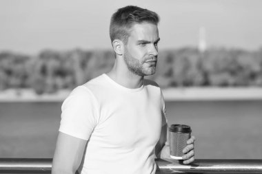 Basit bir yaz eğlencesi. Genç adam nehir kıyısında kahve içmekten hoşlanıyor. Yakışıklı adam sıcak bardağı dışarıda tutuyor. Sabah ayini. Kafein enerjisi. İç ve keyfini çıkar. Kahveden sonra hayatın tadını çıkar. Afiyet olsun.