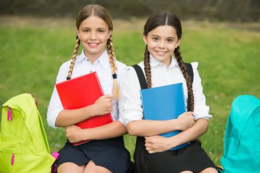 Kitapları ve sırt çantaları olan küçük kızlar. Çocuklar not almak için not defteri tutarlar. Mutlu çocukluk. Okula dönüyorum. Öğrenciler derse hazır. Sınava hazırlan. Açık havada birlikte ders çalışacağız.