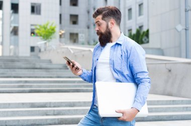 Adam şehir geçmişinde çalışacak. Modern teknoloji. Sosyal uzaklık çağında çalışmak. Dizüstü bilgisayarı olan bir adam boş caddede yürüyor. İş merkezi yeniden açılıyor. Modern hayat. Not defteriyle modern hippi işçi.