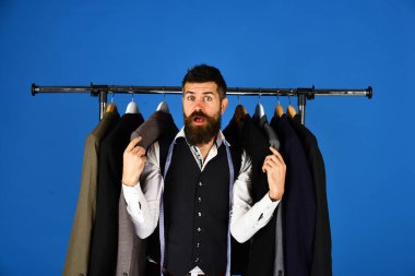 Şaşırmış yüzlü bir terzi ve ceketlerinin içinde mezuralar var.