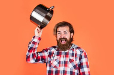 Restorana hoş geldin. İsimsiz dökme demir pişirme kabı. Yapışkan olmayan kaplamalı politetrafluoretilen teflon. Sağlıklı yemek pişirmek. Kareli gömlekli profesyonel aşçı. Sakallı koca